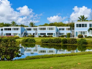 Pale blue and white condo buildings lining a broad green lawn beneath a bright tropical sky.