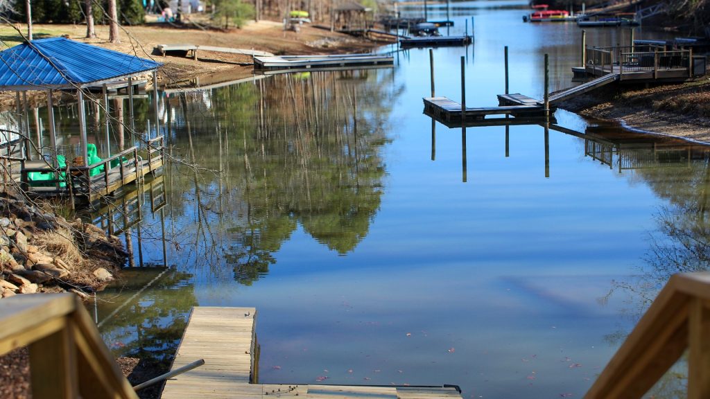 A calm canal with wooden docks and boats along the shore, reflections of trees on the water.