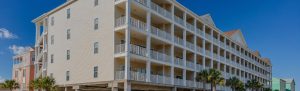 Beige multi-story beachfront condo with white balconies and palm trees against a clear blue sky.
