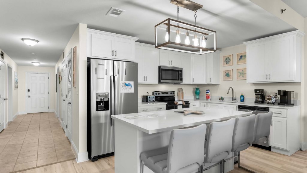 Bright modern kitchen with white cabinets, stainless steel fridge and microwave, and a large island with gray stools.