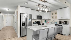 Bright modern kitchen with white cabinets, stainless steel fridge and microwave, and a large island with gray stools.