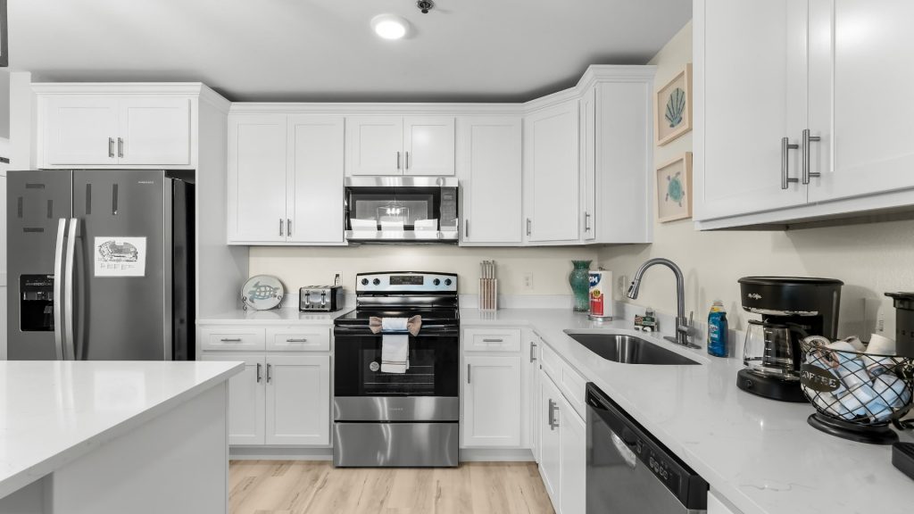 Bright white U-shaped kitchen with stainless steel fridge, oven, and microwave, white countertops, and a sink along the right wall.