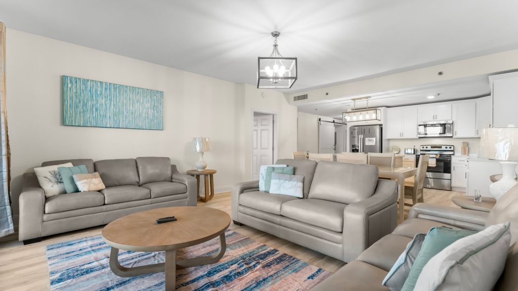 Open-concept living room and kitchen with gray leather sofas, teal pillows, and a blue abstract painting on the wall.