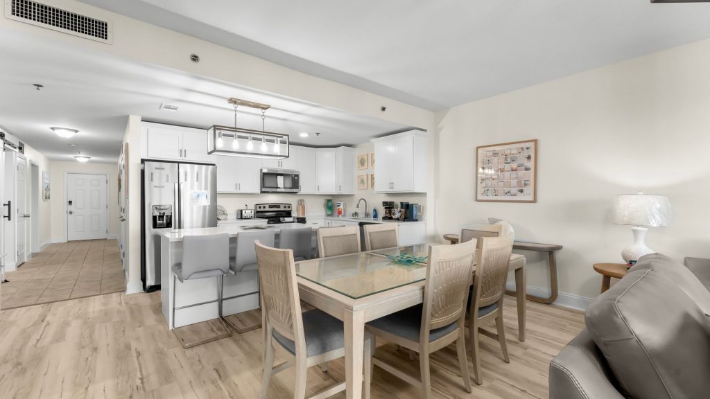 Open-concept kitchen and dining area with white cabinets, stainless steel refrigerator, and glass-top dining table with wooden chairs.