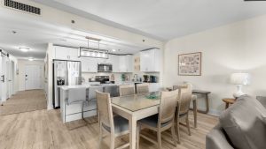 Open-concept kitchen and dining area with white cabinets, stainless steel refrigerator, and glass-top dining table with wooden chairs.