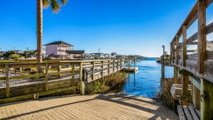 murells-inlet-upscaled | Swack Vacations Wooden boardwalk along a canal with houses, a palm tree, and calm blue water under a clear sky