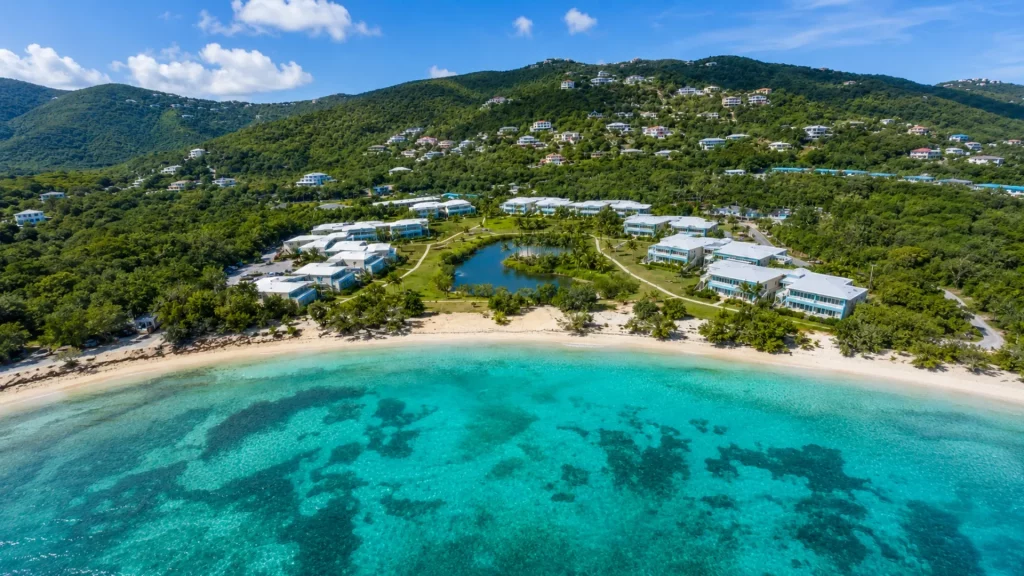 Aerial view of Sapphire Beach Resort with beachfront condo buildings, landscaped grounds, turquoise water and green hills.