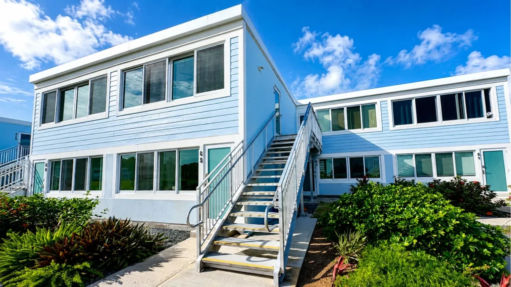 Two-story light-blue apartment building with white trim and a central metal staircase outside. 3D perspective under a bright blue sky.