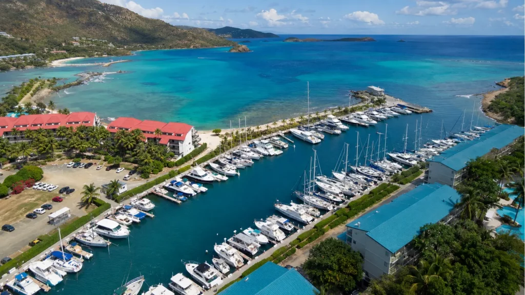 Aerial view of sailboats and powerboats docked at Sapphire Beach Marina, surrounded by clear water, tropical buildings, beaches, and green hills.