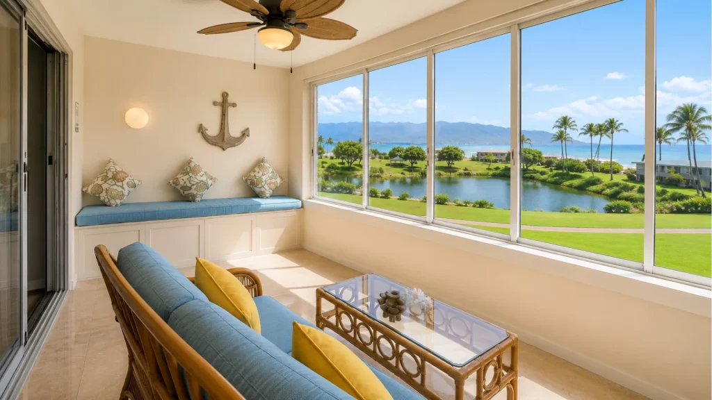 Cozy sunlit balcony seating area with blue cushions and a glass coffee table, overlooking palm trees and a oceanfront landscape through large windows