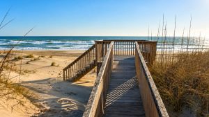 Wooden boardwalk leading to a sandy beach and blue ocean under a clear sky.