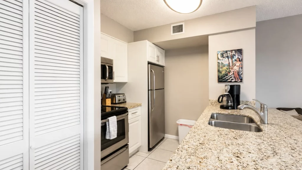 Modern kitchen with white cabinets, granite countertops, and stainless steel fridge and stove, plus a Cuban poster on the wall