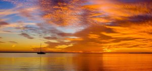 Silhouette of a sailboat on calm water against a vibrant orange and blue sunset sky.