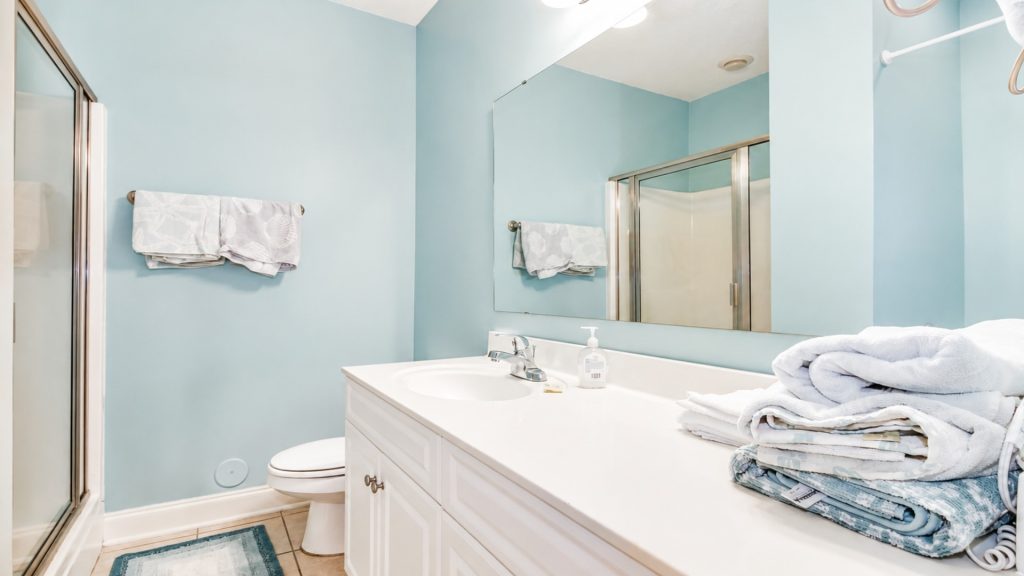 Bright bathroom with light blue walls, white vanity, and stacked towels on the counter near the sink.