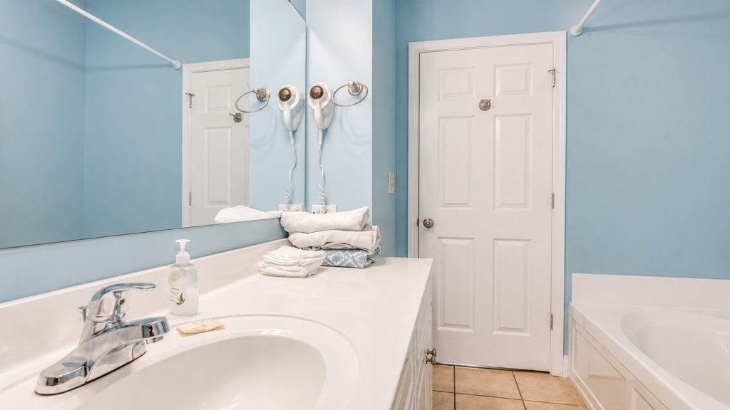 Bright blue bathroom with white double sink, large mirror, towel stack, and wall-mounted hair dryers.