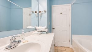 Bright blue bathroom with white double sink, large mirror, towel stack, and wall-mounted hair dryers.