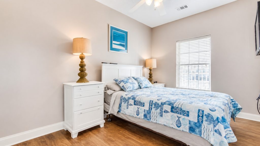 Bedroom with a white headboard and two matching nightstands, blue patterned quilt, and warm lamps on each side.
