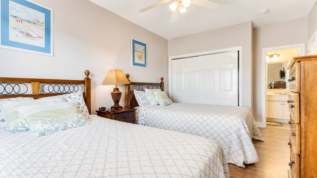 Two twin beds with white quilts and matching pillows in a bright hotel room, between them a wooden nightstand with a lamp.
