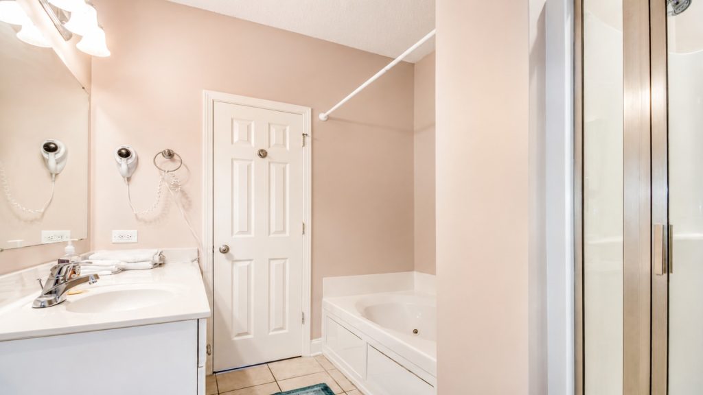 Bathroom with beige walls, white vanity and sink, mirror, and wall-mounted hair dryer next to outlets and towels on the counter on the left.