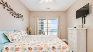 Coastal bedroom with seashell-pattern quilt and aqua pillows, right by a sliding glass balcony door showing the ocean view