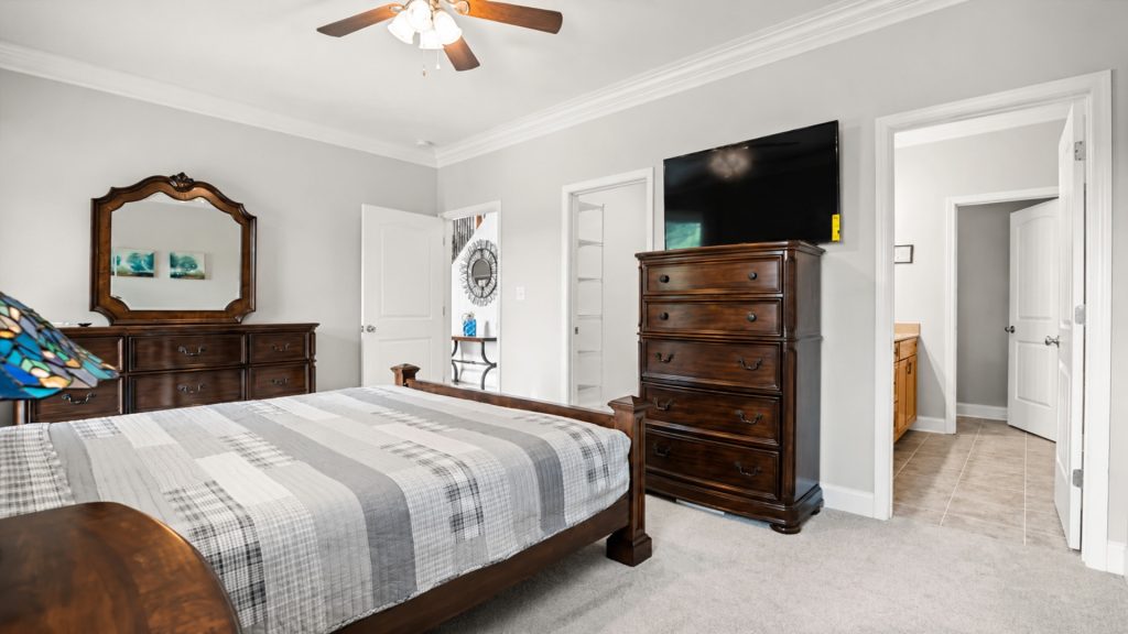 Bedroom with dark wood dresser and matching mirror, large bed with plaid bedding, and ceiling fan above.