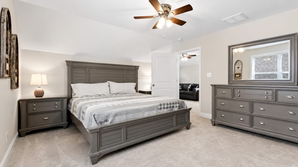 Grey wood master bedroom with a large bed, two matching nightstands, and a dresser in a neutral-toned room with beige carpet.