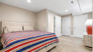 Cozy bedroom with a striped red, blue, and yellow bedspread and light wood furniture against beige walls