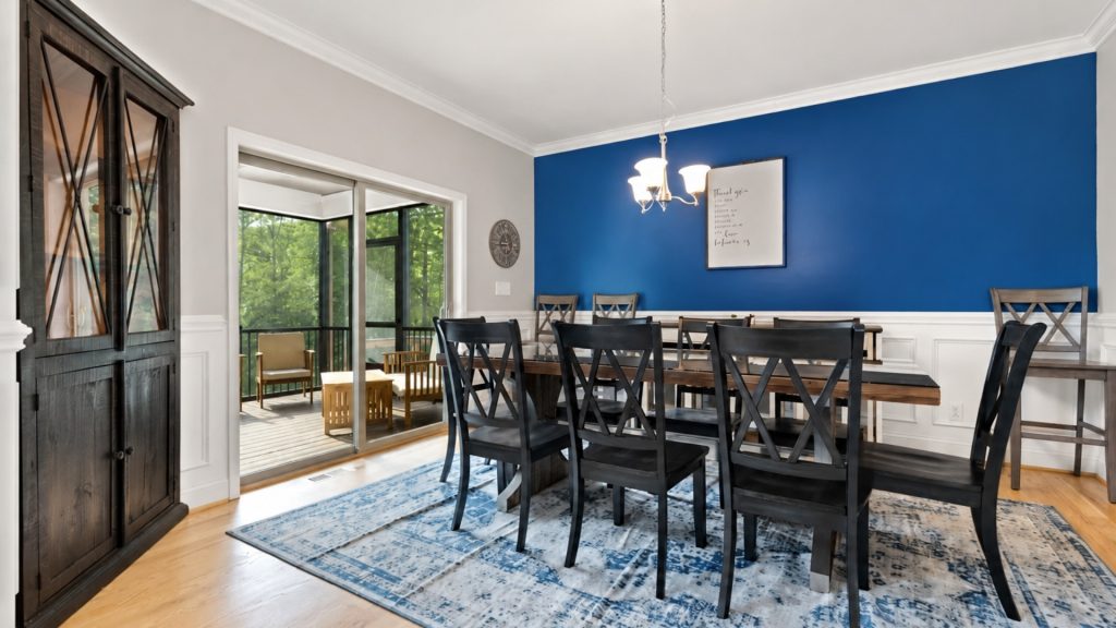 Dining room with a blue accent wall, dark wood table and black chairs, chandelier, and white wainscoting.