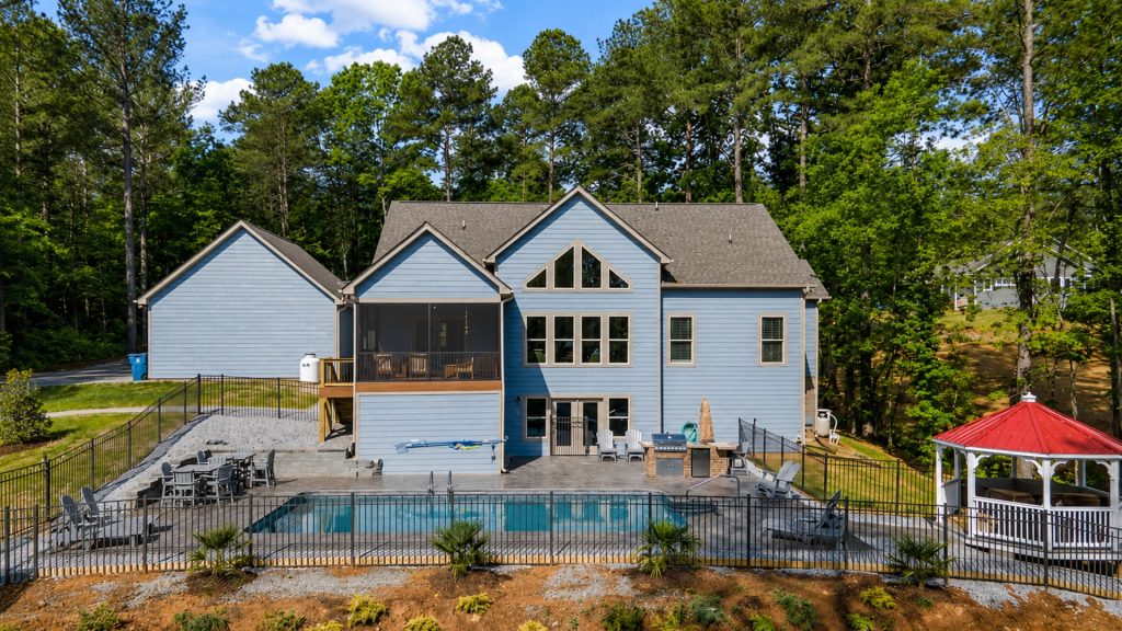 Blue two-story house with pool and fenced patio, surrounded by trees and outdoor seating areas.