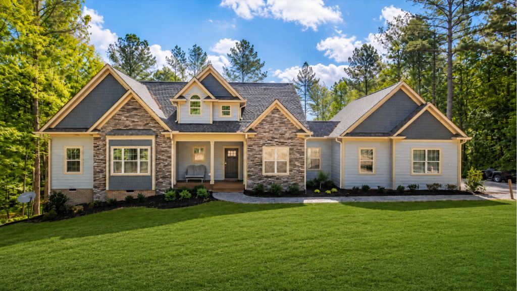 Modern family home with blue siding and stone facade, front porch, and dormer windows amid a green lawn and tall trees.