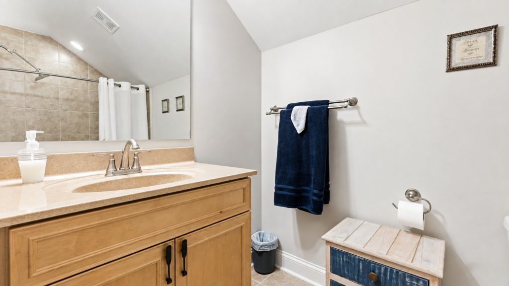 Vanity area with beige countertop, wooden cabinet, and sink; navy towels on a wall rack and framed wall art nearby.