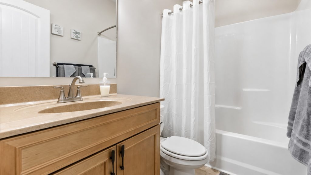 Bathroom with a tan countertop sink, wooden vanity, and white bathtub with a shower curtain.