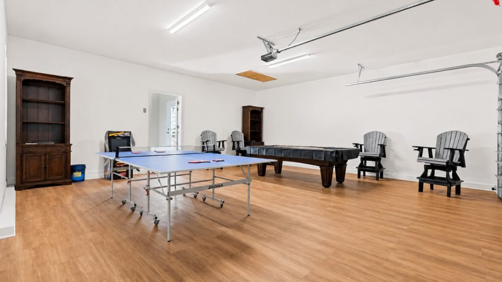 Recreation room with a blue ping-pong table, a dark pool table, tall wooden cabinets, and several Adirondack chairs on a wooden floor