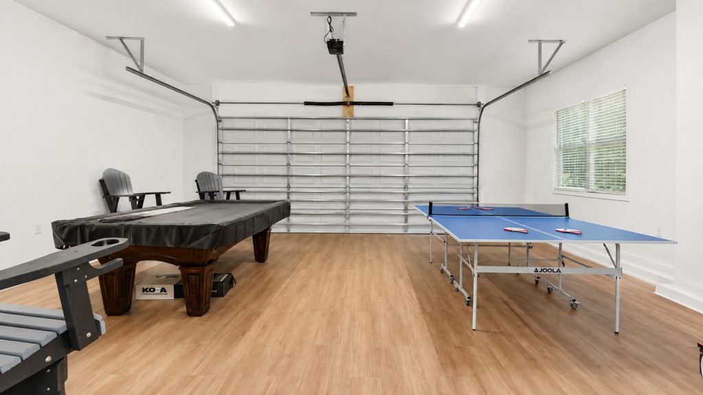 Bright home recreation room with a pool table covered in black cloth and a blue ping-pong table nearby on a wood floor.