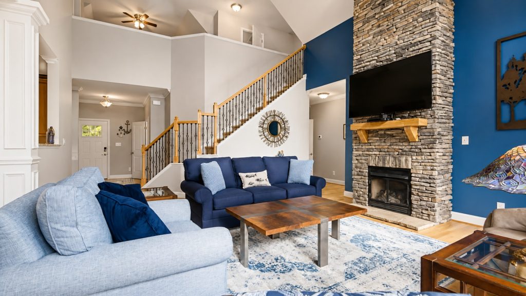 Bright living room with a stone fireplace and blue accent wall, a mounted TV, and navy-blue sofas around a wooden coffee table.