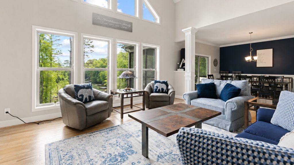 Bright living room with large windows overlooking a green wooded yard; navy-blue and gray seating with elephant cushions.