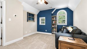 blue-bayou-interior-5 | Swack Vacations Cozy living area with a dark blue accent wall, arched window, tall bookshelf, and gray sofa with a lamp and pillows.