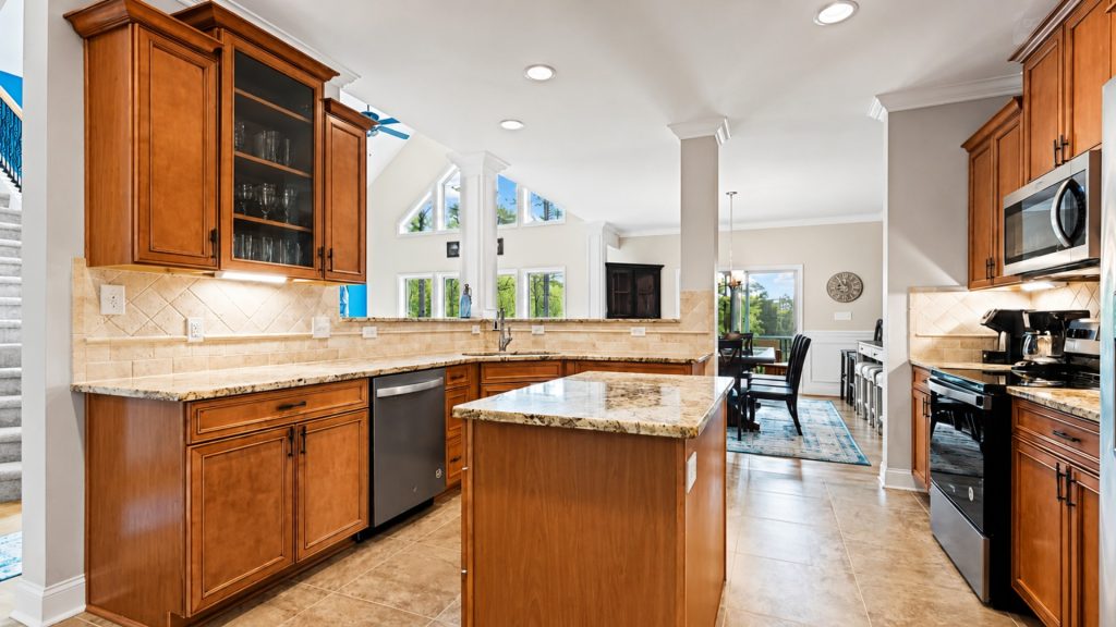 Open kitchen with warm wooden cabinets, granite island, and stainless appliances; dining area visible in background.
