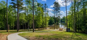 blue-bayou-tile-background | Swack Vacations Curving concrete path through a pine forest toward a lake with docks and a gazebo under a blue sky.