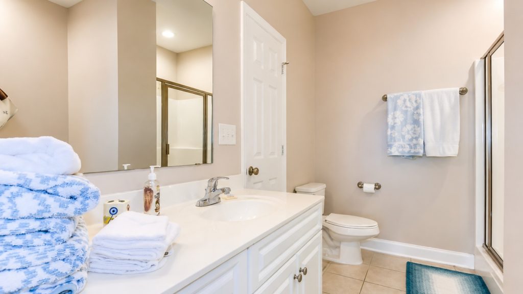 Bright beige bathroom with a white vanity, stacked blue towels, and a toilet nearby.
