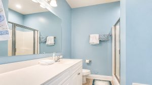 cherry-208-bath-3 | Swack Vacations Blue bathroom with white vanity, large mirror, soap dispenser, and towels on a rack beside a glass shower.