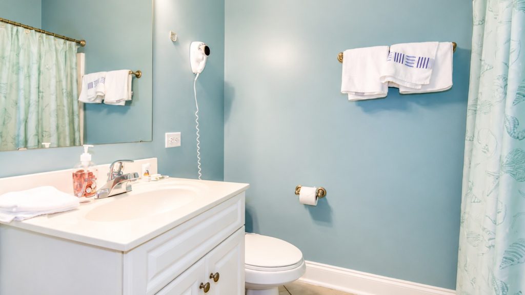 Blue bathroom with a white vanity, sink, and mirror; a wall-mounted hair dryer above the outlet on the blue wall.