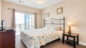Bedroom with a metal-framed bed and a shell-pattern quilt, opening to a balcony through sliding glass doors.