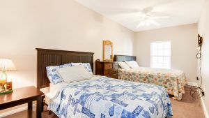 Bright hotel room with two beds, coastal-print quilts, a wooden dresser with a mirror, and a ceiling fan.