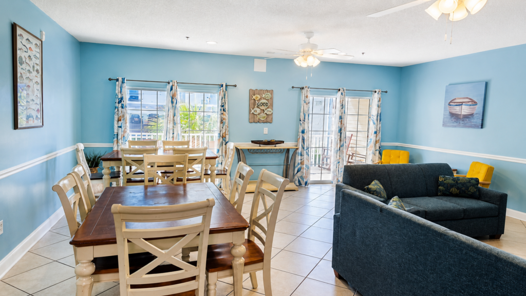 Bright coastal-style dining and living area with blue walls, cream chairs, and a navy sofa.