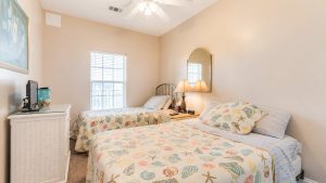 cherry-208-king-double | Swack Vacations Twin bedroom with seashell-pattern bedspreads, matching pillows, and a nightstand between beds with two lamps.