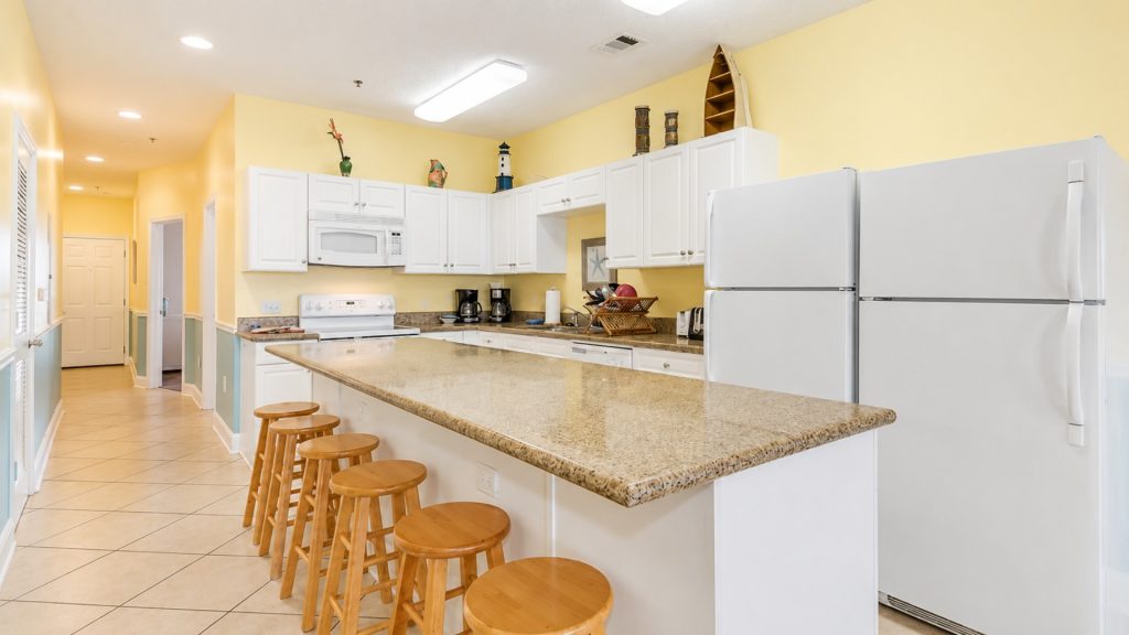 Bright kitchen with white cabinets, beige granite island, and yellow walls; wooden bar stools line the island.