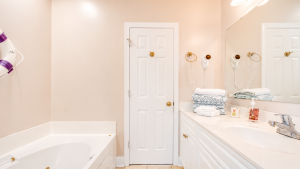 Bright bathroom with a white bathtub on the left and a white double-sink vanity on the right, door centered in peach walls, towels stacked on the counter