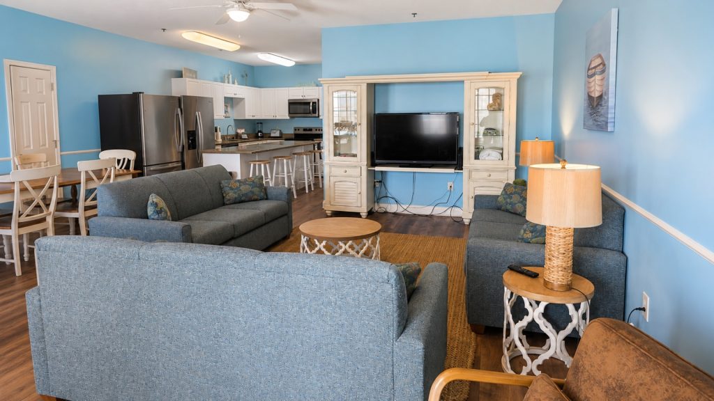 Open-plan living room and kitchen with blue walls, white cabinets, a stainless steel fridge, and a TV in a beige entertainment cabinet.
