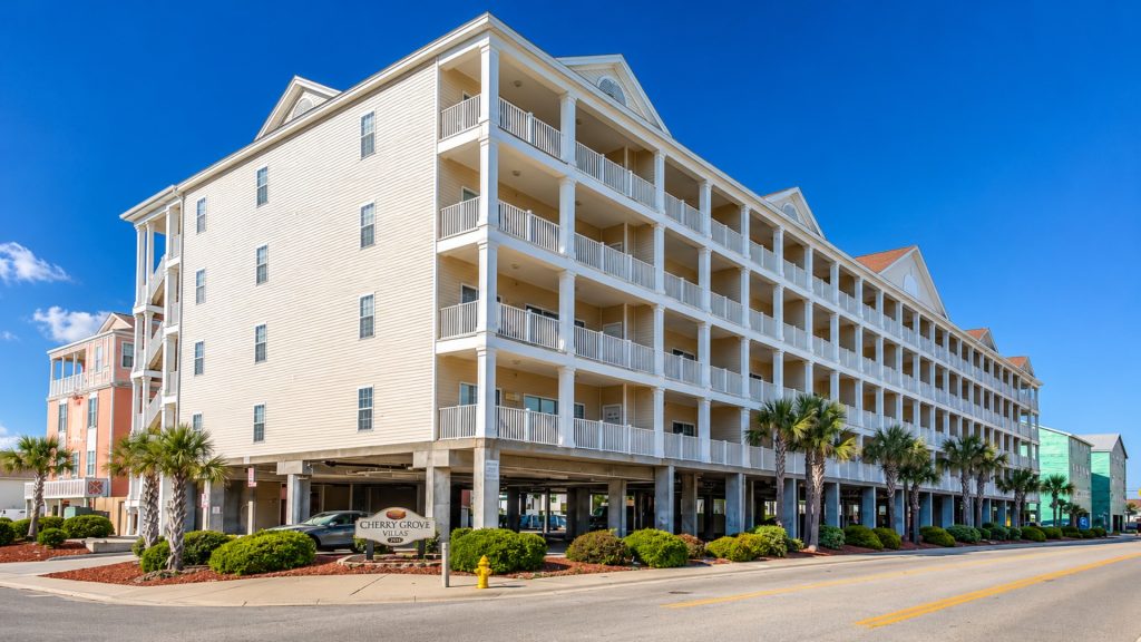 Beachfront hotel with multiple white balconies and a clear blue sky; palm trees line the street in front. (Hotel exterior)